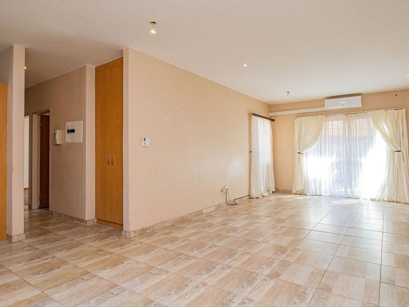 Spacious, empty living area featuring neutral tiled flooring, built-in storage cupboards, and a wall-mounted air conditioning unit with access to a sliding glass door.