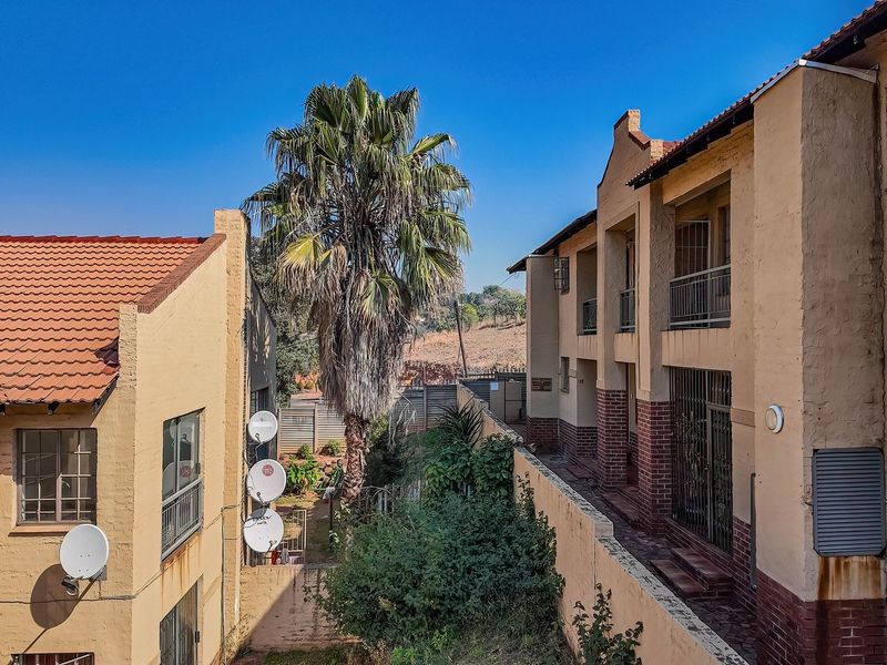 Rear view of a townhouse complex featuring terracotta tiled roofs, brick facade detailing, and private balconies with security gates.