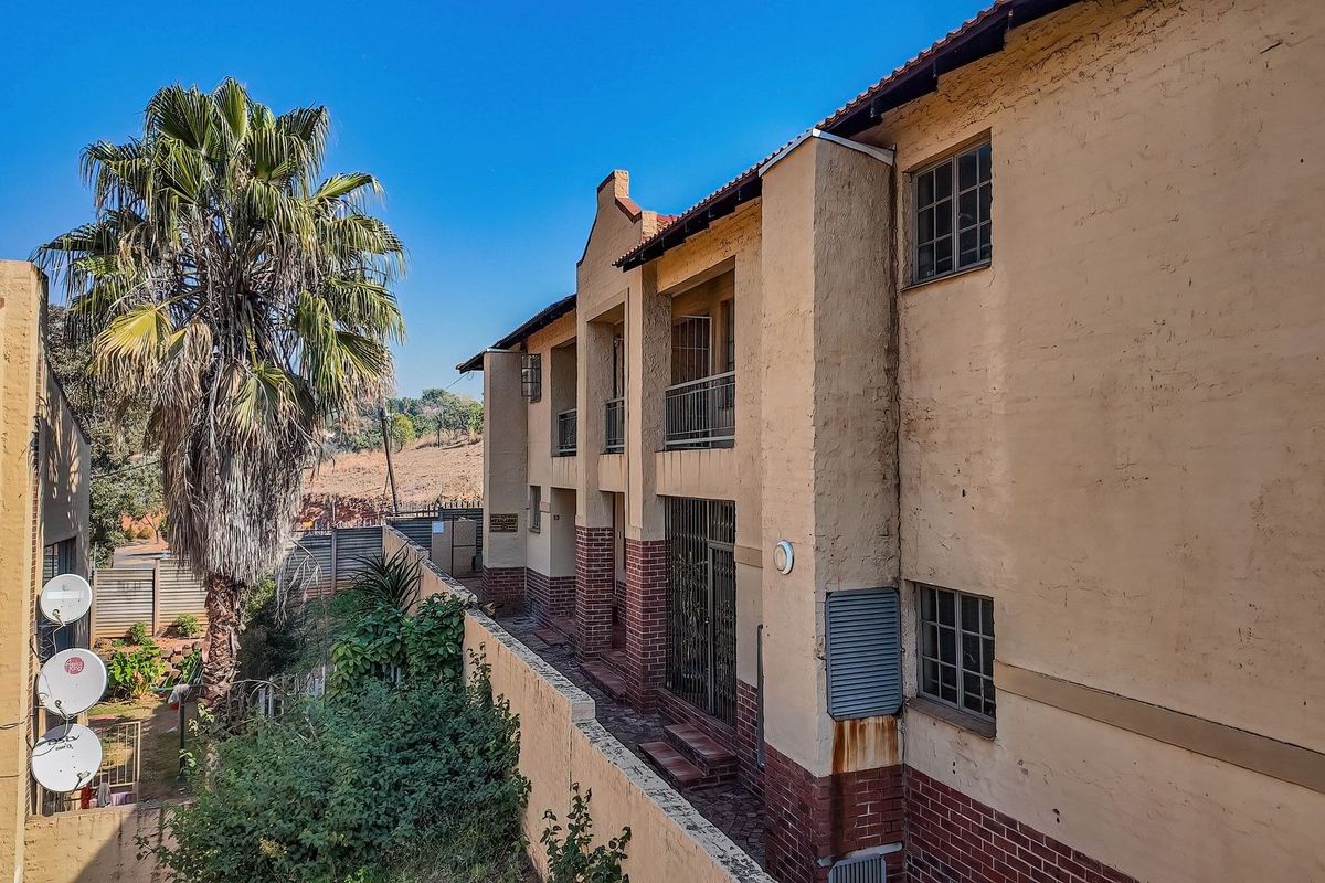 Rear elevation of a multi-story townhouse complex featuring brick and plaster finishes, metal security gates, and balcony access.