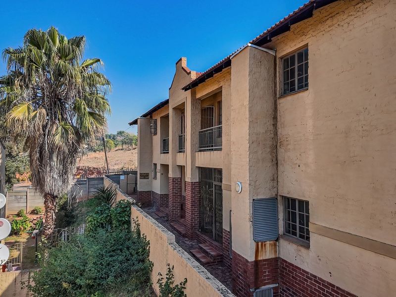 Rear elevation of a multi-story townhouse complex featuring brick and plaster finishes, metal security gates, and balcony access.