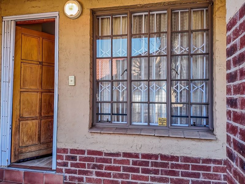 Front entrance area featuring a wooden door, security bars on the window, and a combination of brick and rendered wall finishes.