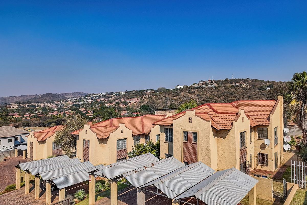 Aerial view of a townhouse complex featuring multiple units with tiled roofs, brick facades, and covered carport parking areas.