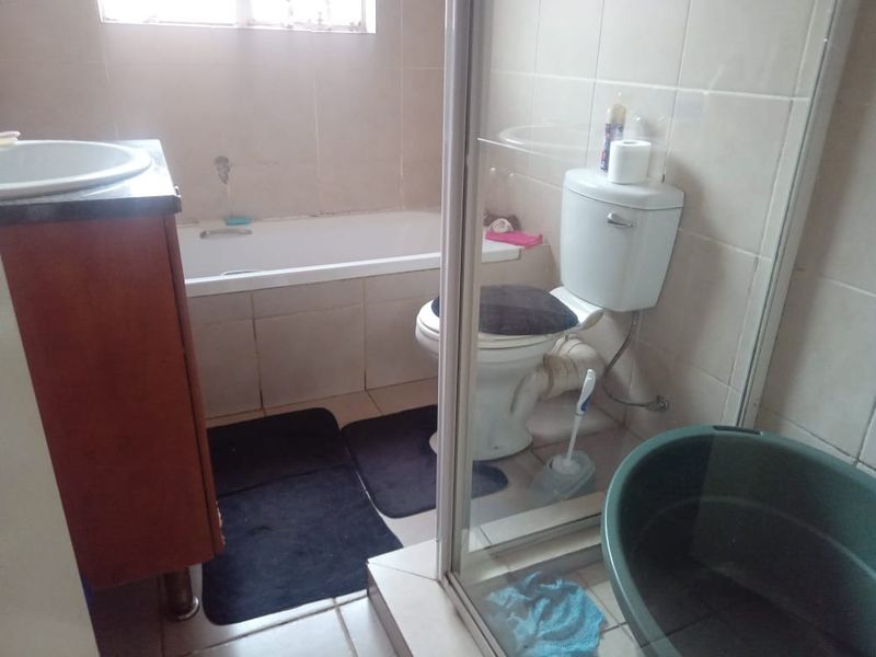 A functional bathroom featuring a bathtub, toilet, and separate shower enclosure with tiled finishes, requiring some cosmetic updates to improve its overall condition.