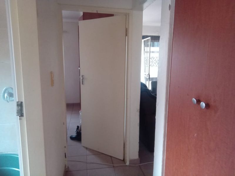 A functional hallway featuring tiled flooring and a built-in cupboard, providing access to adjacent rooms within the home.