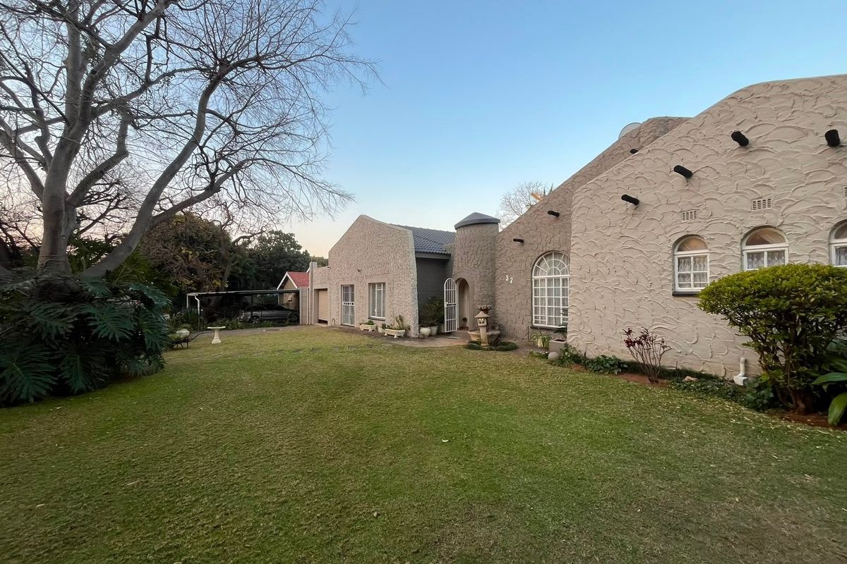 A view of the rear exterior of the house featuring a textured facade, arched windows, and a well-maintained lawn with a carport.