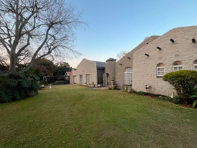 A view of the rear exterior of the house featuring a textured facade, arched windows, and a well-maintained lawn with a carport.