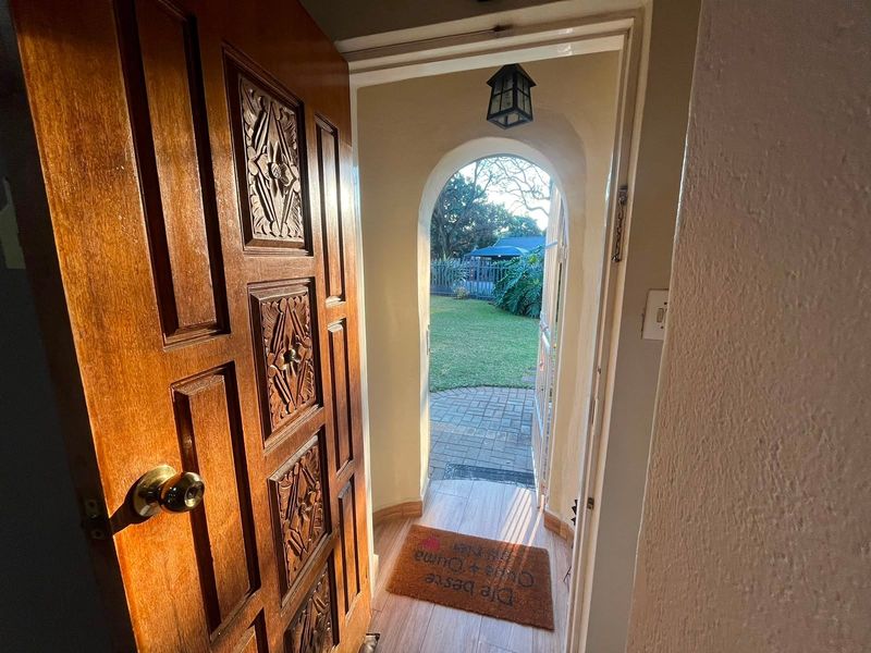 An inviting entryway featuring a decorative carved timber door, arched transition, and tiled flooring leading out to a garden area.