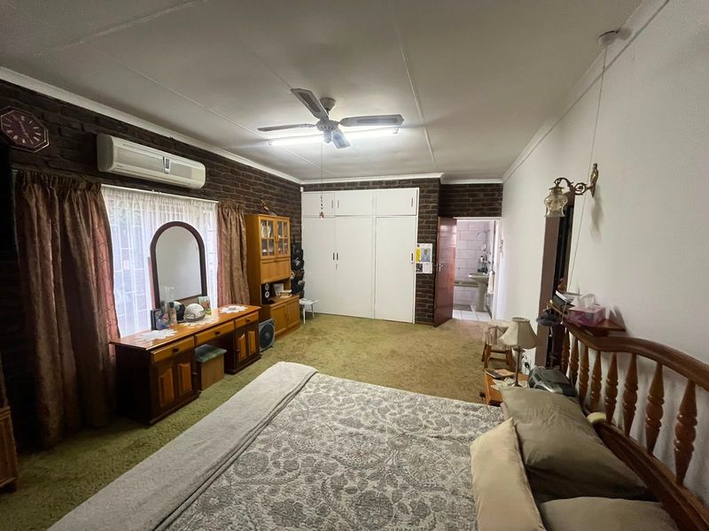 Spacious bedroom featuring built-in cupboards, exposed brick wall, ceiling fan, and split-system air conditioning, with direct access to an en-suite bathroom.