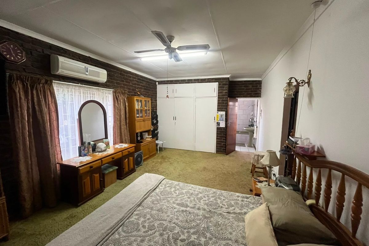 Spacious bedroom featuring built-in cupboards, exposed brick wall, ceiling fan, and split-system air conditioning, with direct access to an en-suite bathroom.