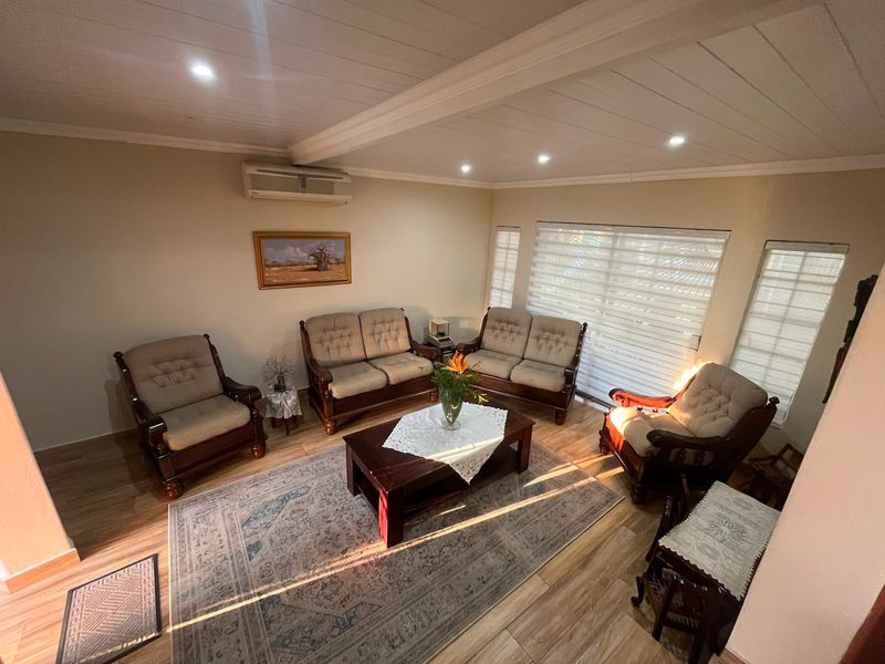 A well-maintained living room featuring laminate flooring, recessed downlighting, and a wall-mounted split-system air conditioner, offering a comfortable and functional space.