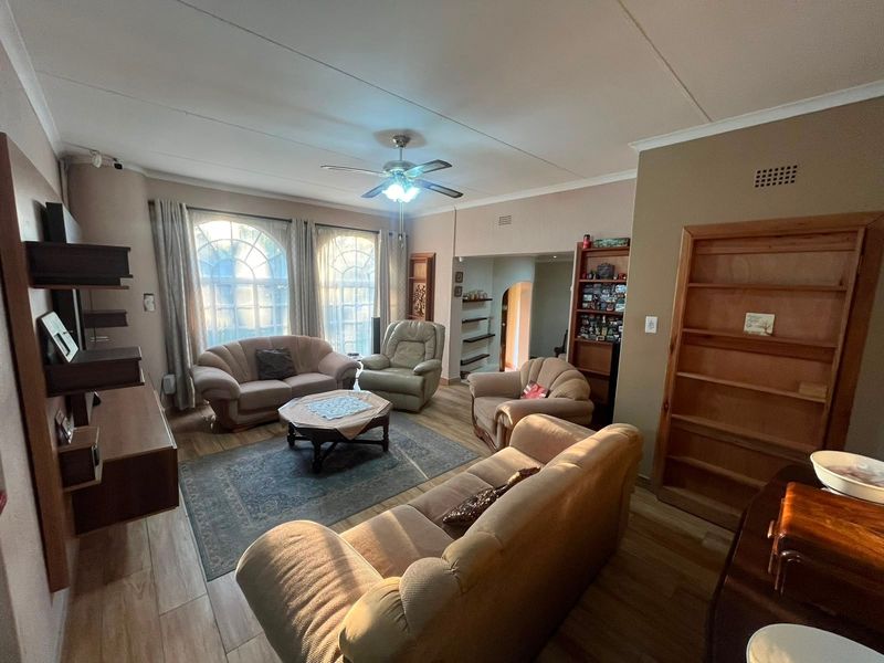 Spacious living room featuring arched windows, laminate flooring, a ceiling fan, and built-in shelving units.