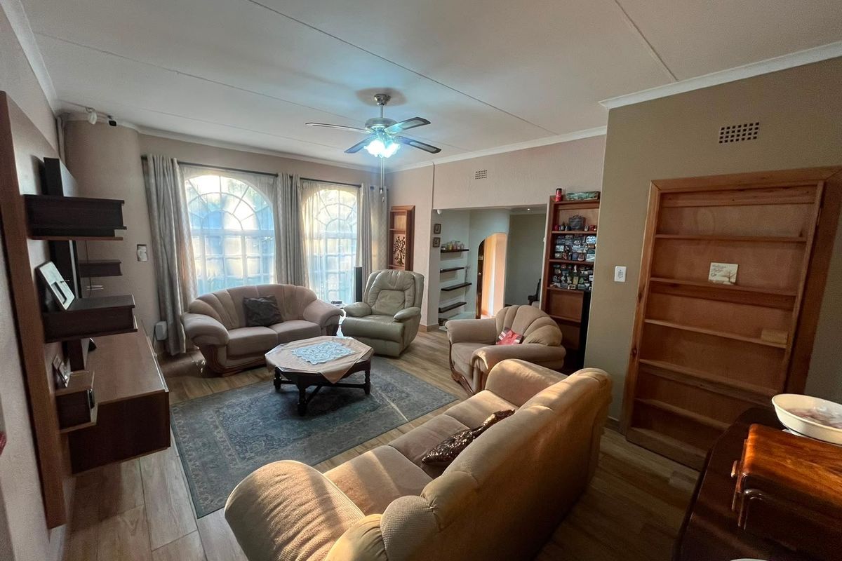 Spacious living room featuring arched windows, laminate flooring, a ceiling fan, and built-in shelving units.