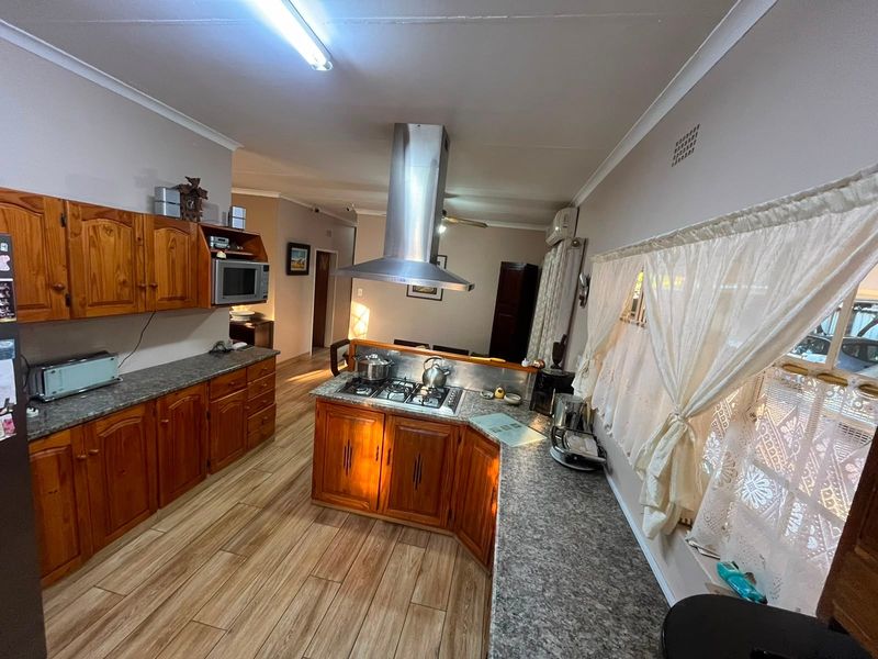 Open-plan kitchen featuring wooden cabinetry, granite countertops, a gas hob with stainless steel extractor, and laminate flooring, flowing into the adjacent living area.