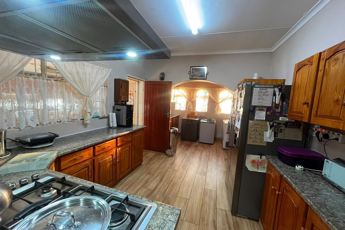 A functional kitchen featuring wooden cabinetry, laminate countertops, a gas hob with extractor fan, and wood-look laminate flooring.