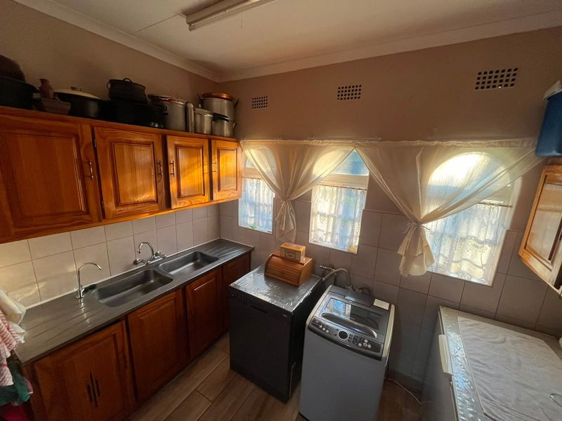 A functional scullery featuring wooden cabinetry, a double stainless steel sink, tiled splashbacks, and dedicated space for laundry appliances.