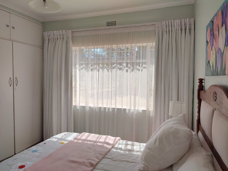A cozy bedroom featuring built-in cupboards, a window with security bars, and neutral wall finishes, offering a comfortable and functional living space.