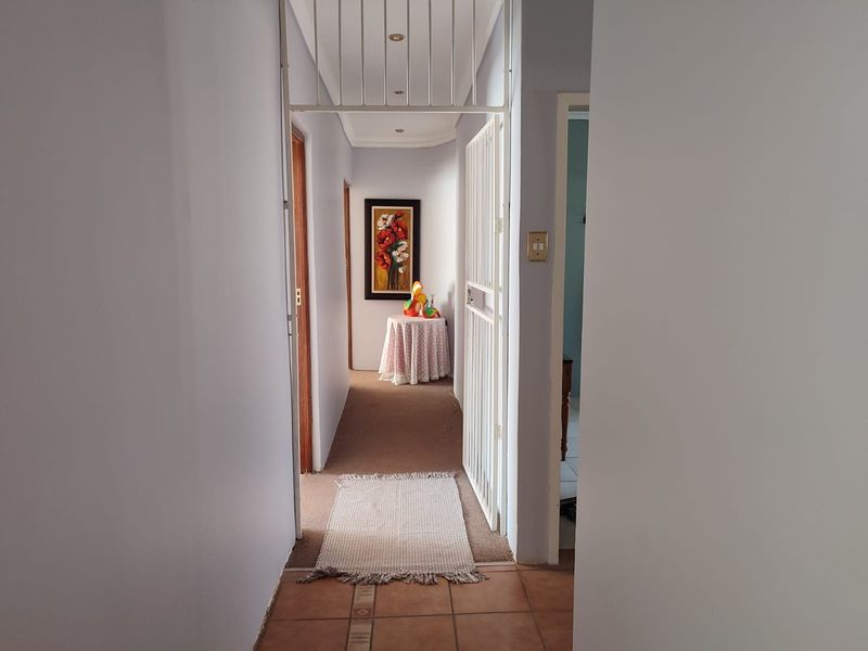 A functional hallway connecting living spaces, featuring a security gate, recessed lighting, and a mix of tiled and carpeted flooring.