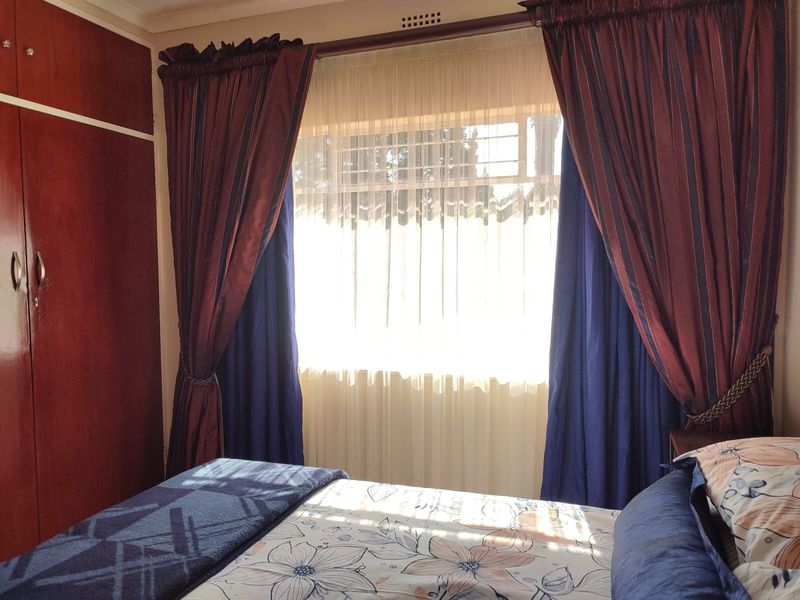 A bedroom featuring a built-in wooden wardrobe and a window with security bars, providing natural light and storage space.