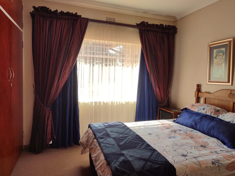 A well-maintained bedroom featuring built-in wardrobes, carpeted flooring, and a window with layered curtains.