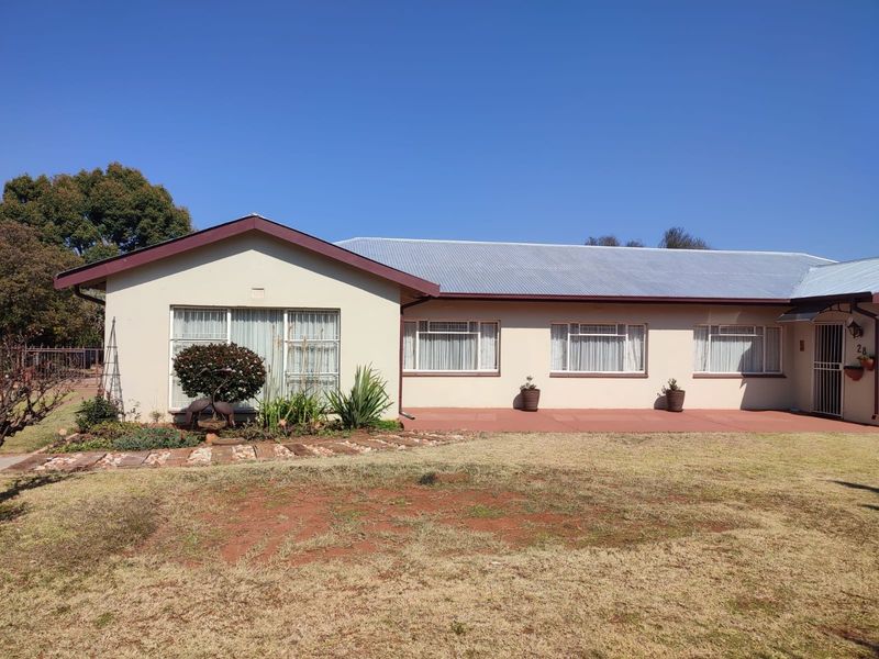 Front elevation of a single-story house featuring a corrugated metal roof, plastered walls, a concrete patio, and a paved garden path.