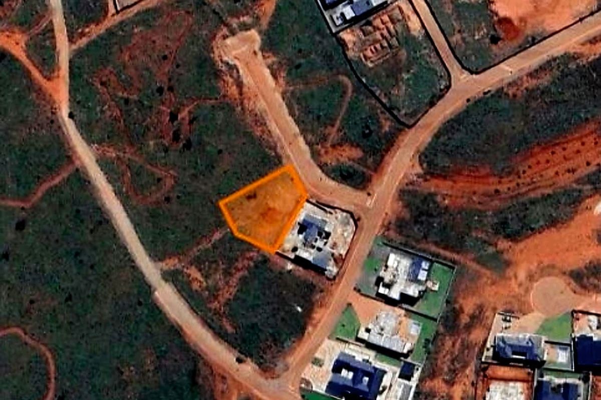 An aerial view of a vacant residential land plot highlighted in orange, situated within a developing neighborhood with established road access.