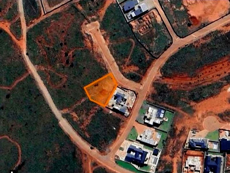 An aerial view of a vacant residential land plot highlighted in orange, situated within a developing neighborhood with established road access.
