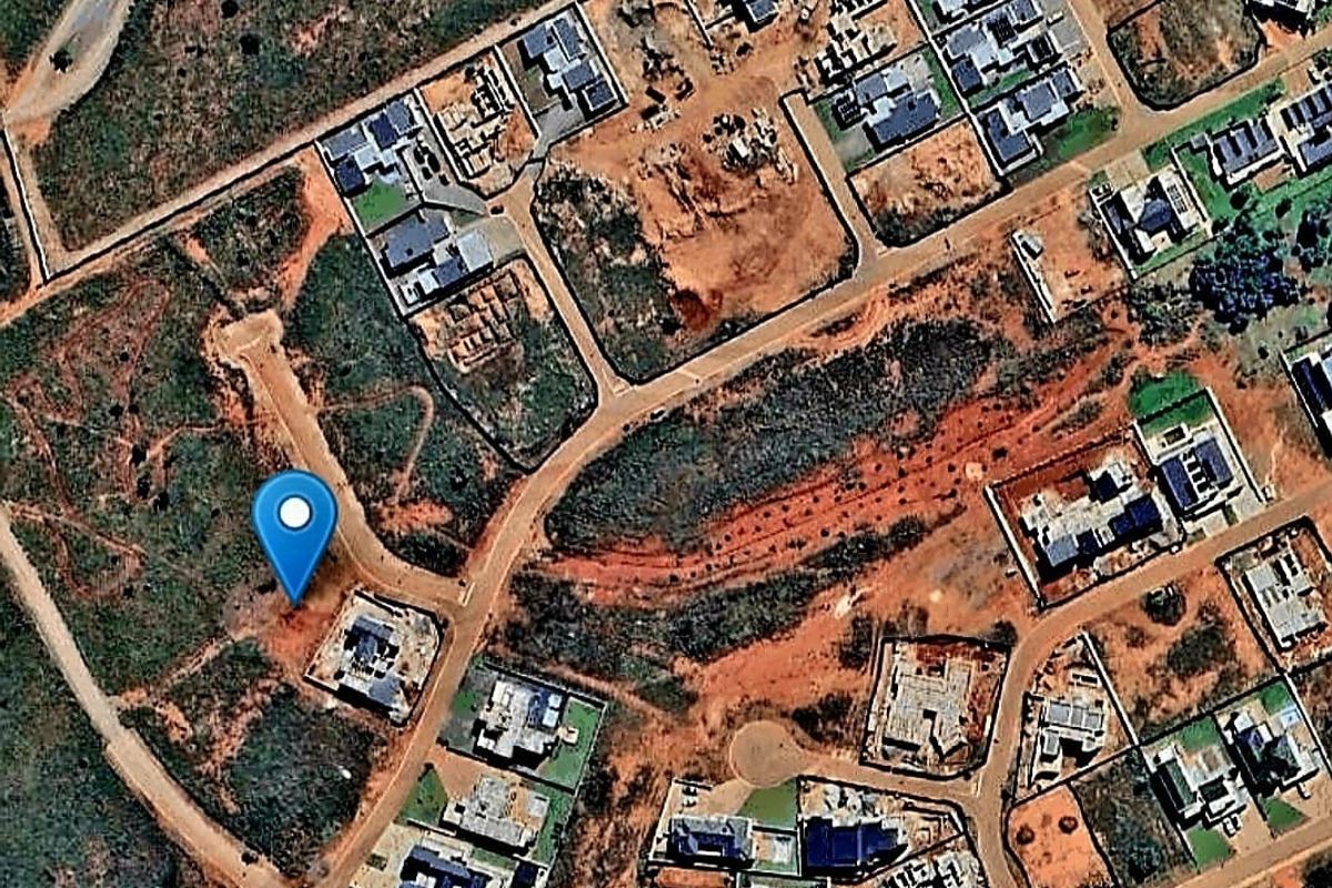 An aerial view of a vacant residential plot situated within a developing neighborhood, featuring road access and proximity to existing residential properties.
