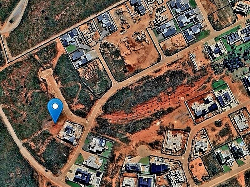 An aerial view of a vacant residential plot situated within a developing neighborhood, featuring road access and proximity to existing residential properties.