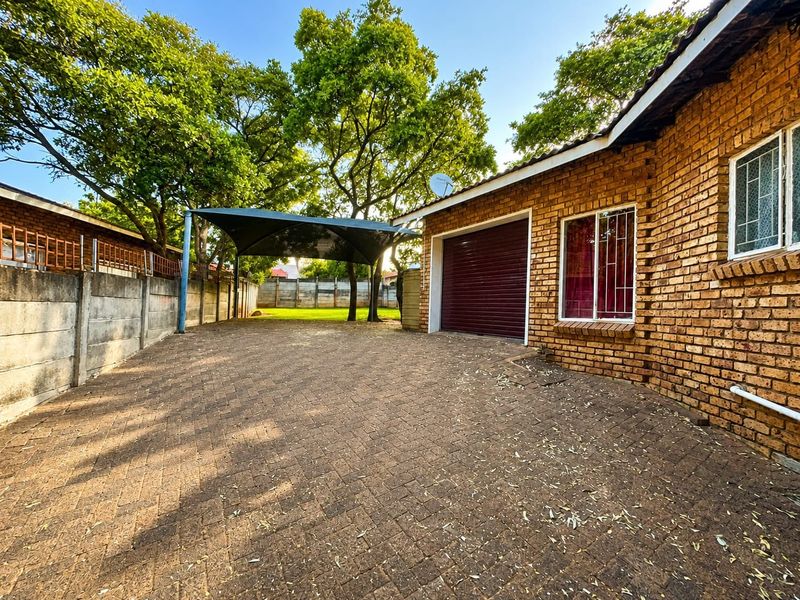 Exterior view of the property featuring a brick facade, paved driveway, garage, and a shade sail structure in the front yard.