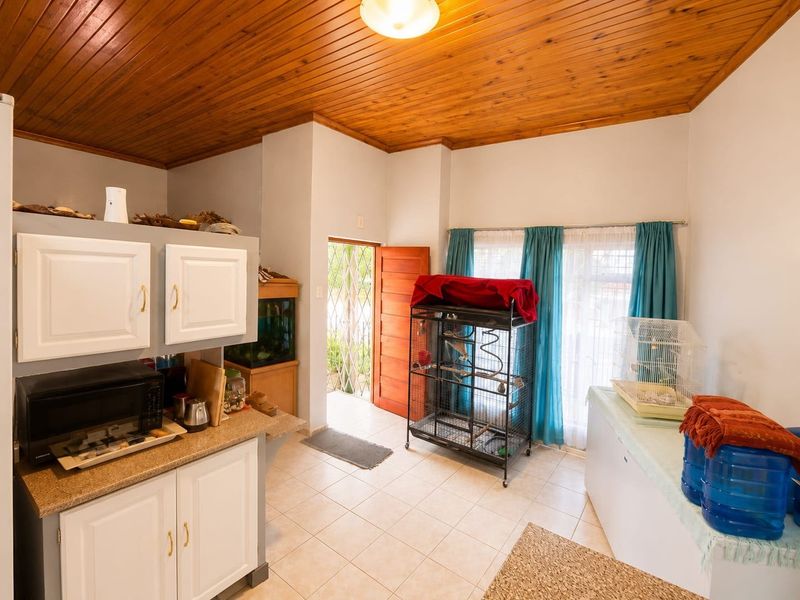A functional kitchen area featuring white cabinetry, granite-look countertops, and a distinctive timber tongue and groove ceiling, with direct access to the exterior.