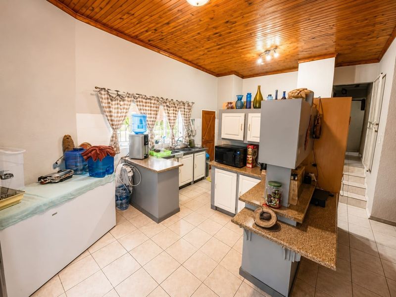 A functional kitchen featuring granite countertops, built-in cabinetry, a double sink, and a distinctive timber-paneled ceiling with tiled flooring throughout.