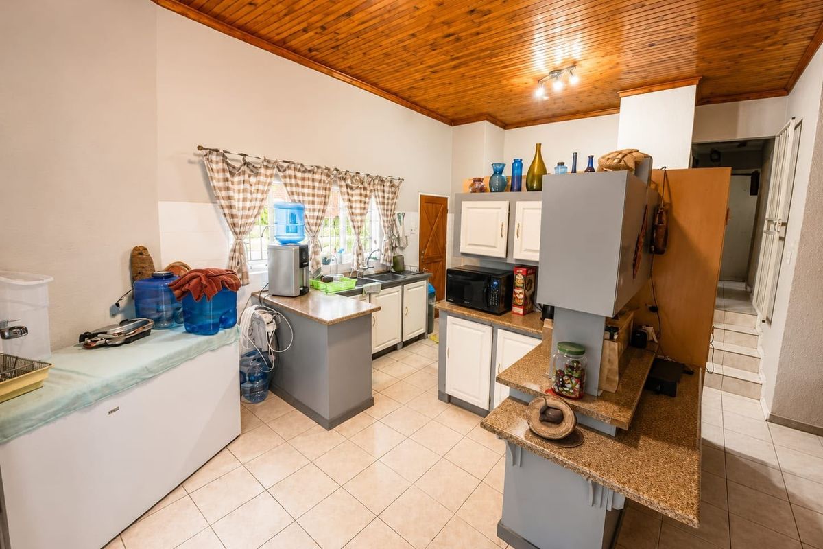 A functional kitchen featuring granite countertops, built-in cabinetry, a double sink, and a distinctive timber-paneled ceiling with tiled flooring throughout.