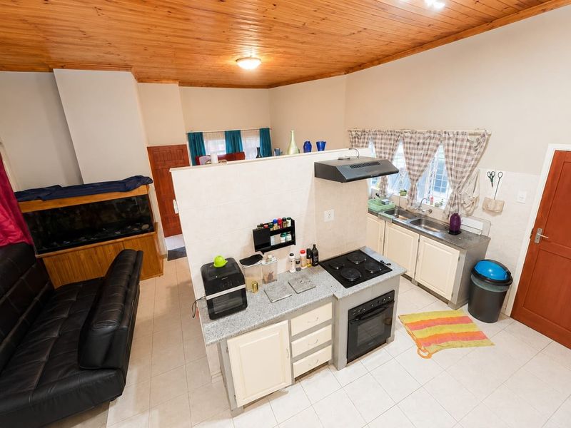 Open-plan kitchen and living area featuring a timber ceiling, tiled floors, granite countertops, and built-in cabinetry with integrated cooking appliances.