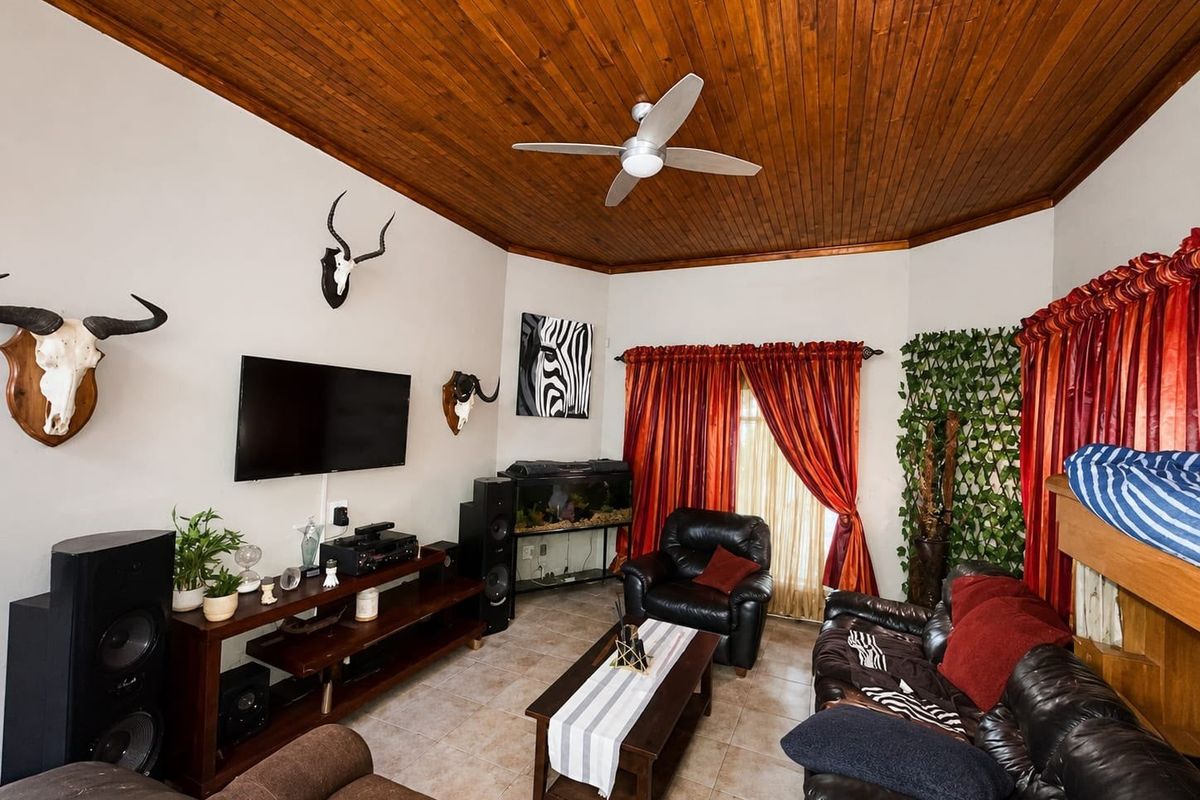 A living room featuring a vaulted timber tongue and groove ceiling, ceiling fan, tiled flooring, and access to the outdoors via a sliding glass door.