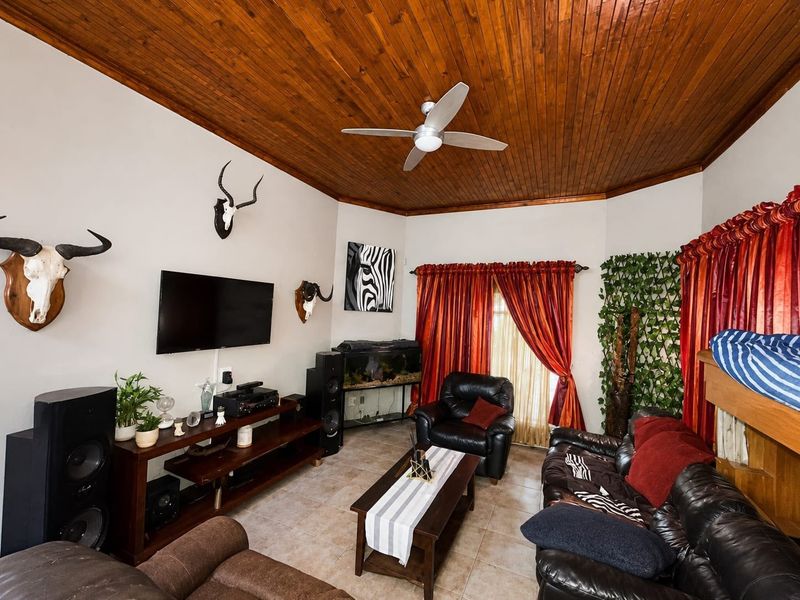 A living room featuring a vaulted timber tongue and groove ceiling, ceiling fan, tiled flooring, and access to the outdoors via a sliding glass door.