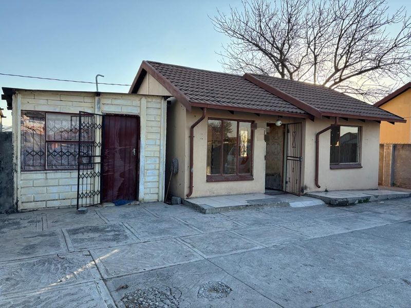 Front exterior view of a single-story house featuring a tiled roof, security gates, and a paved driveway area.
