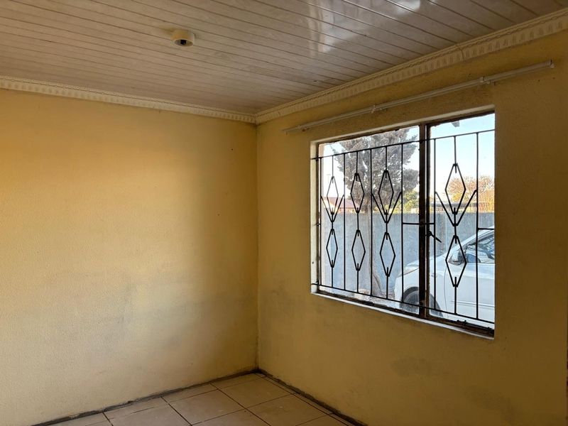 An empty living room featuring tiled flooring, a tongue and groove ceiling, and a window fitted with security bars.
