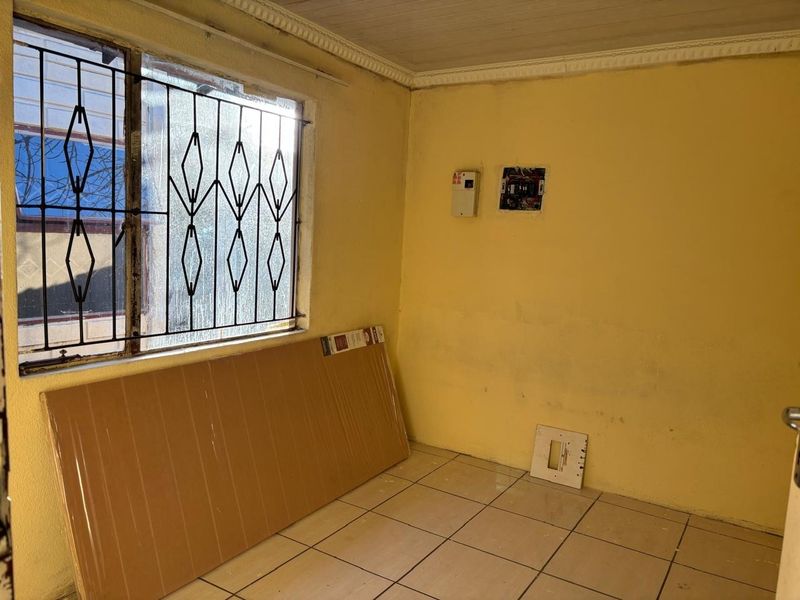 An empty room featuring tiled flooring, security bars on the window, and exposed electrical infrastructure requiring maintenance and cosmetic updates.