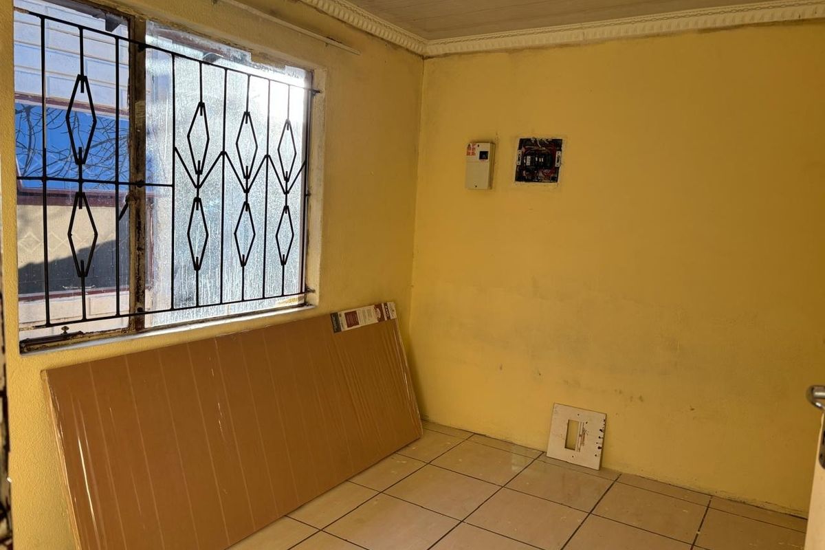 An empty room featuring tiled flooring, security bars on the window, and exposed electrical infrastructure requiring maintenance and cosmetic updates.