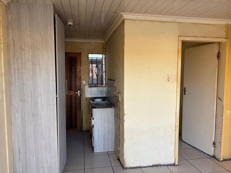 A compact, empty kitchen area featuring basic cabinetry, a sink, and tiled flooring, requiring cosmetic updates and wall repairs.