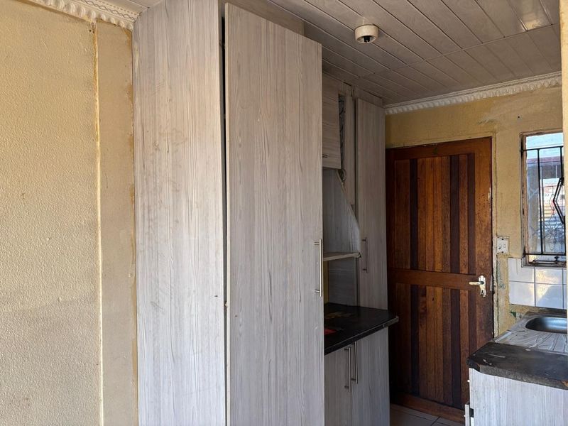 A compact kitchen area featuring built-in cabinetry, laminate countertops, and a stainless steel sink, requiring cosmetic updates to the walls and ceiling.