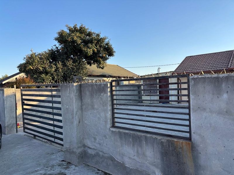 Front exterior view of the property featuring a concrete boundary wall with metal security gates, spiked security topping, and a paved driveway.
