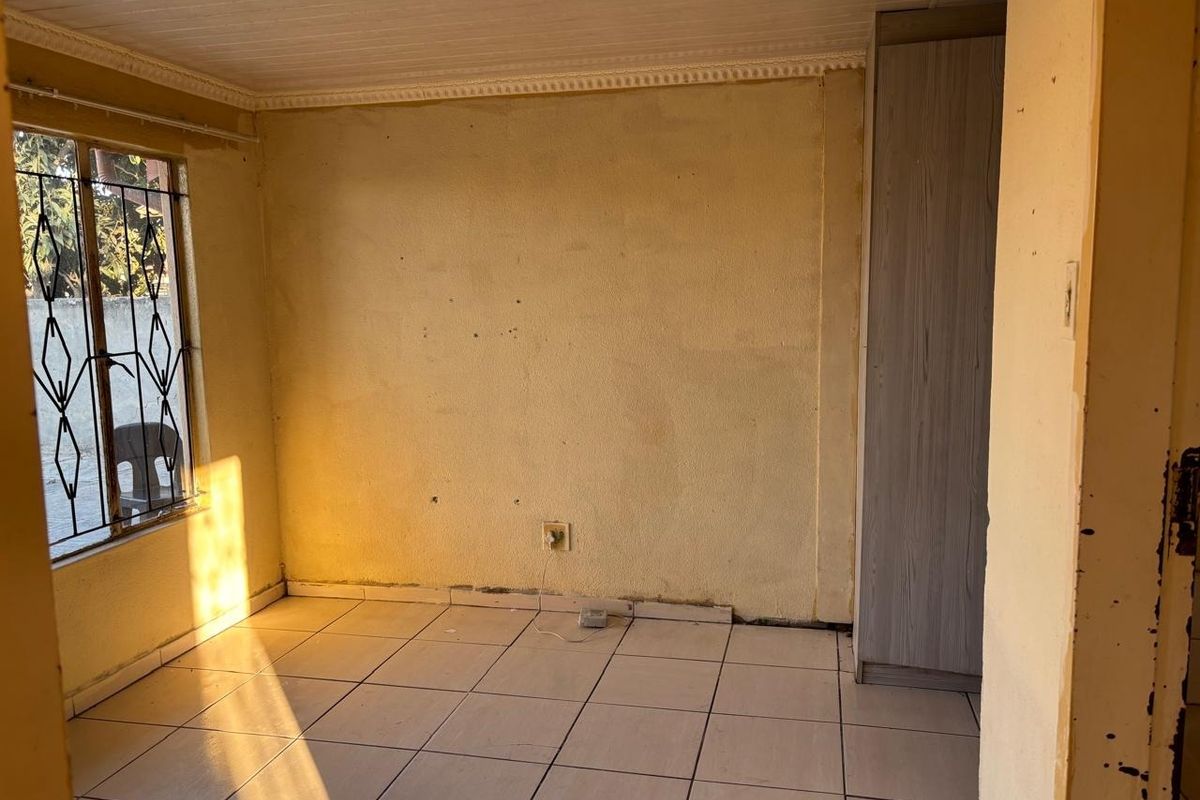 An empty bedroom featuring tiled flooring, a built-in wardrobe, and security bars on the window, awaiting cosmetic updates to refresh the space.