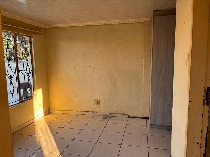 An empty bedroom featuring tiled flooring, a built-in wardrobe, and security bars on the window, awaiting cosmetic updates to refresh the space.