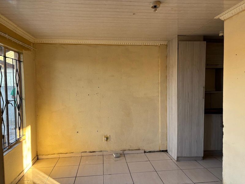 An empty open-plan living area featuring tiled floors, a built-in cupboard, and a timber ceiling, requiring cosmetic updates to the wall finishes.