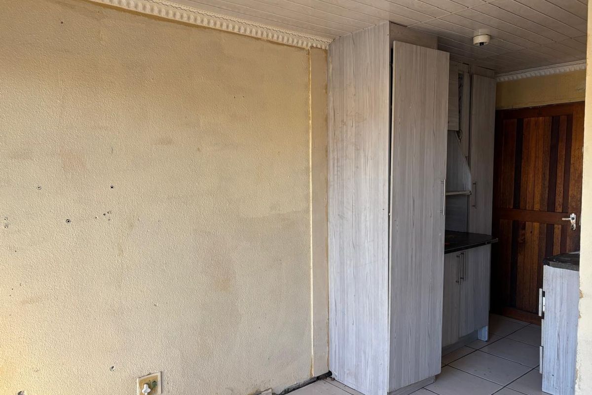 A compact kitchen area featuring built-in cabinetry and tiled flooring, currently in need of cosmetic refurbishment and wall repairs.