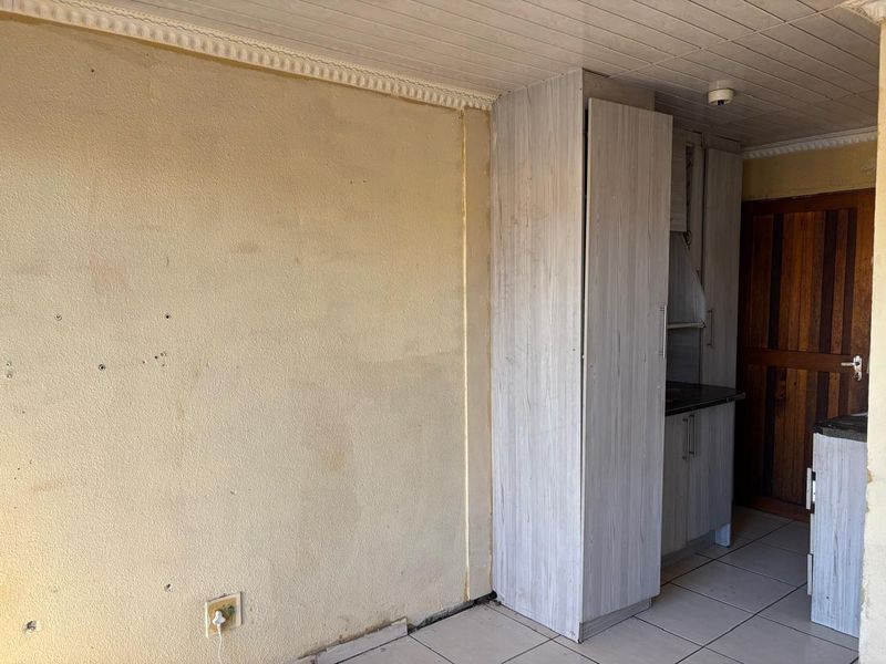 A compact kitchen area featuring built-in cabinetry and tiled flooring, currently in need of cosmetic refurbishment and wall repairs.