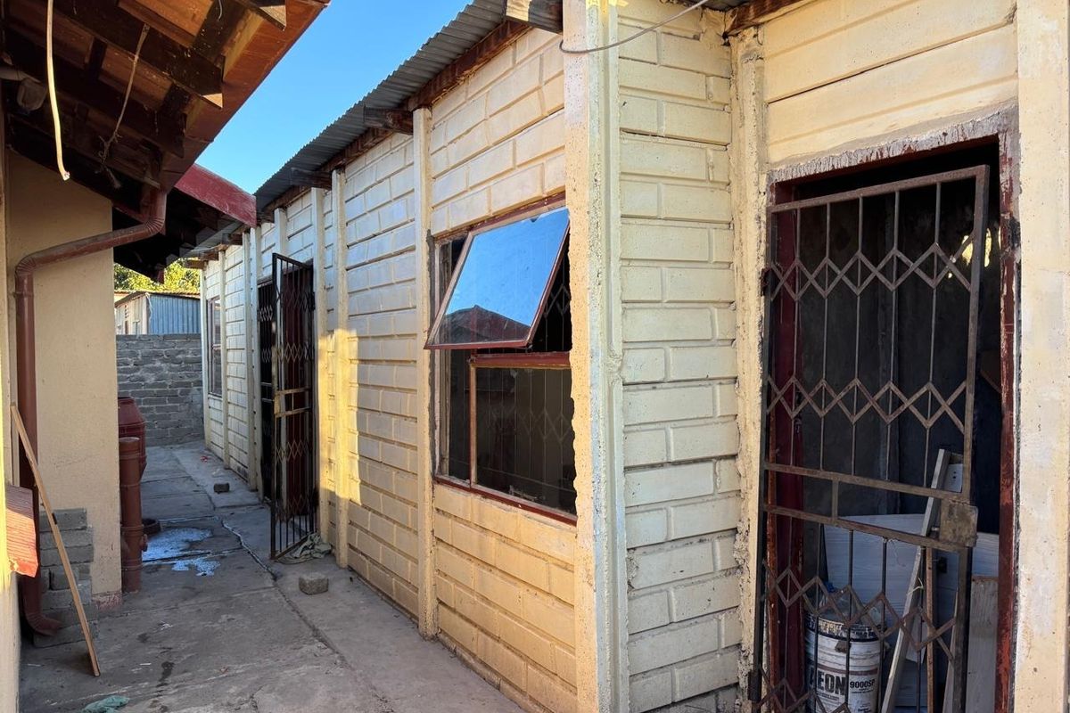 Rear exterior view of the property showing masonry walls, security gates, and a concrete pathway along the side of the building.