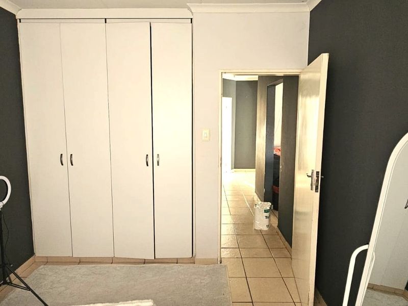 A bedroom featuring built-in wardrobes, tiled flooring, and a doorway leading to a hallway.