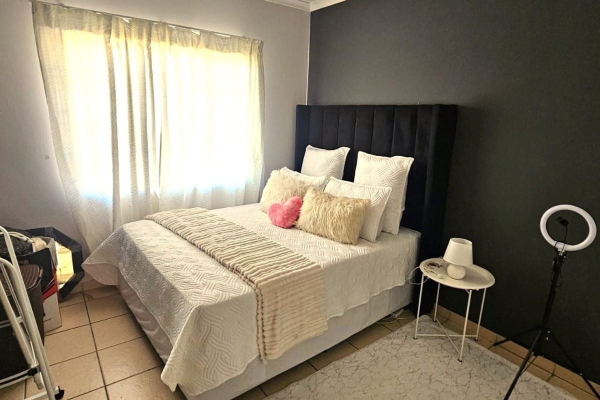A well-maintained bedroom featuring tiled flooring, a dark accent wall, and natural light through window curtains.